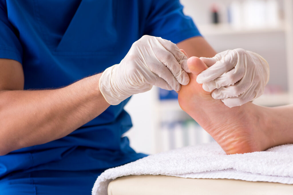 Gloved clinician examining the underside of a patient’s feet in a medical setting